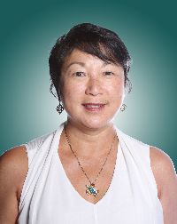 Portrait of a smiling woman with short dark hair, wearing a white blouse and a necklace, set against a gradient teal background.