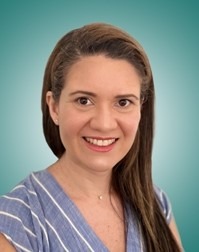 Smiling woman with long brown hair, wearing a blue striped top, poses against a teal background. Suitable for a professional profile or personal introduction.